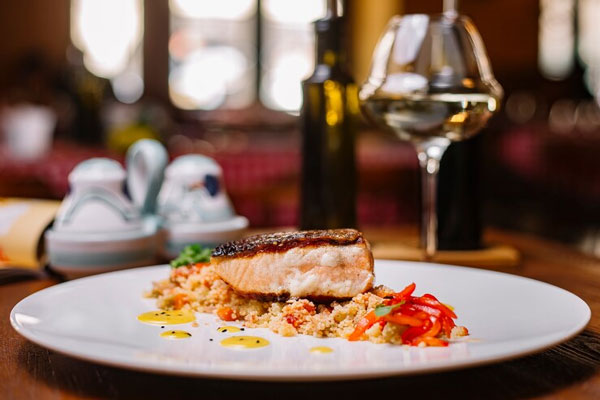 Salmón a las finas hierbas servido sobre un plato blanco con una copa de vino de fondo