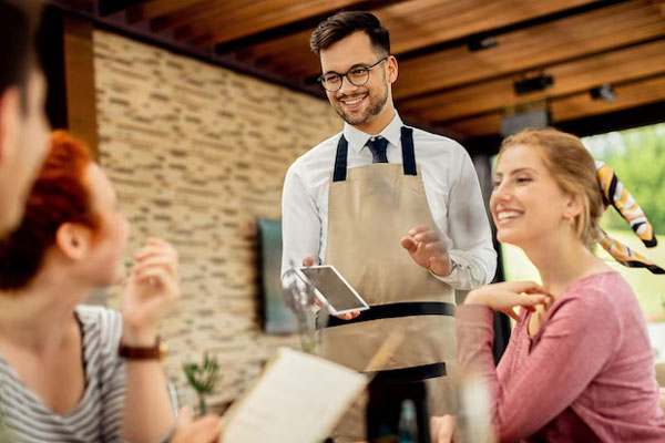 Restaurantes - Mesero toma el pedido de unos clientes con una amplia sonrisa