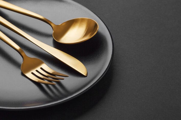 Plato negro sobre una superficie con cubiertos elegantes encima