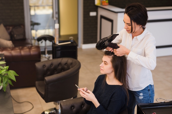 Estilista trabajando en el cabello de una influencer, utilizando un secador para conseguir un pelo sedoso y brillante