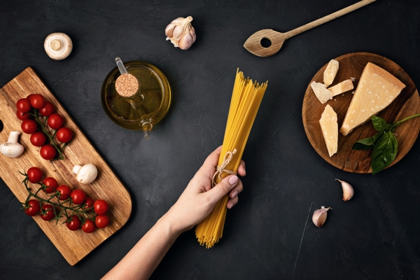 Mujer sosteniendo una ración de spaghetti sobre una mesa con queso, aceite y otros ingredientes frescos que caracterizan a la cocina italiana