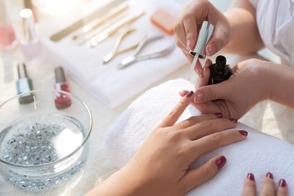 Manicurista pintando las uñas de color rojo, luego de haberlas cortado y limpiado