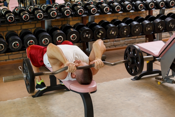 Hombre realizando ejercicios en el banco de musculación que tiene en casa