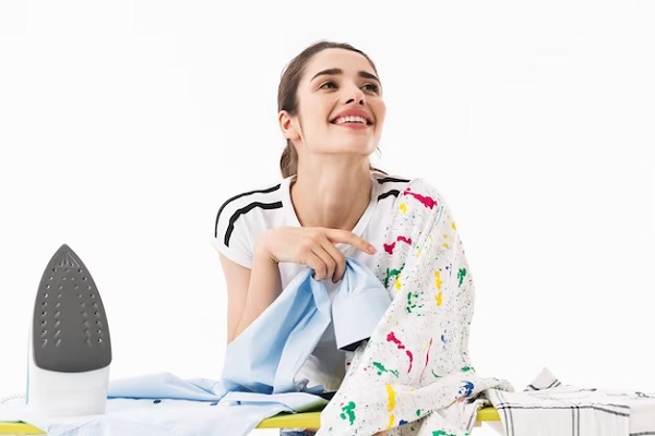 Tinte para ropa- Mujer contenta al preparar las prendas para teñirlas, aplicando calor para eliminar las arrugas y así fije mejor el color