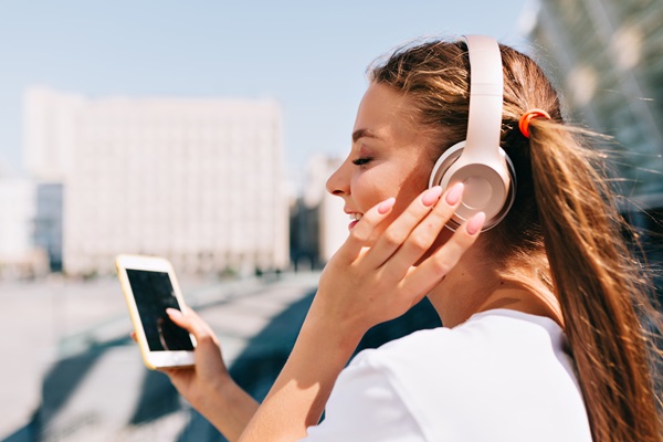 Auriculares inalámbricos - Mujer feliz utilizando unos audífonos Bluetooth, para escuchar su música favorita desde el teléfono sin cables