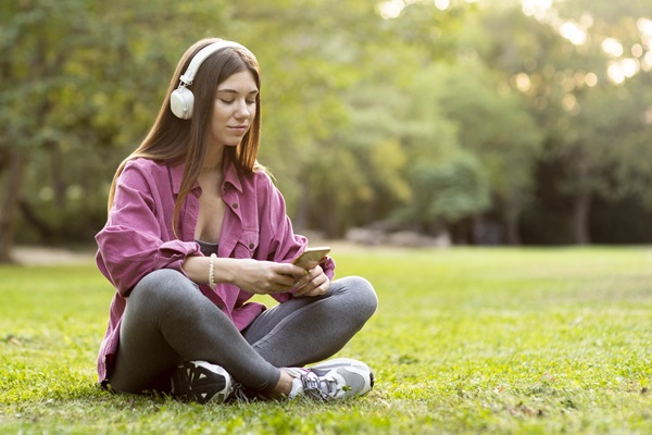 Mujer disfrutando de un tiempo de relajación en el parque, mientras escucha música con unos audífonos Bluetooth