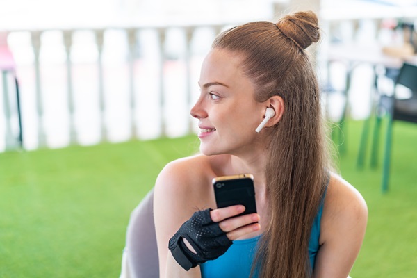 Mujer feliz sosteniendo su teléfono, mientras escucha música de manera cómoda con los audífonos Bluetooth