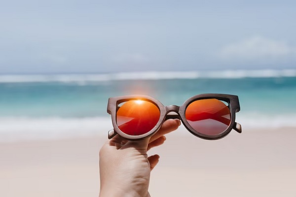 Comprar gafas de sol - Imagen de una persona frente a la playa sosteniendo unas gafas de sol, las cuales ayudan a proteger los ojos de los rayos UV