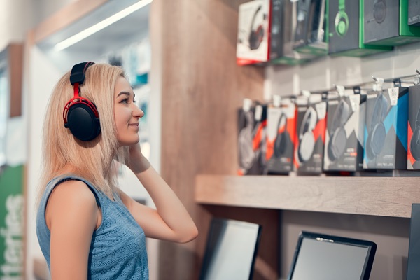 Mujer probando nuevos auriculares en una tienda de electrónica, la cual cuenta con muchos modelos para adaptarse a sus necesidades