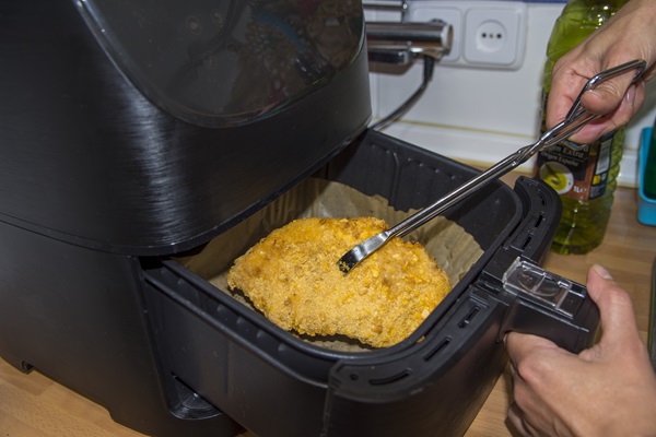 Persona sacando un pieza de pollo crujiente de manera segura, gracias al mango de plástico que tienen las cestas de las freidoras