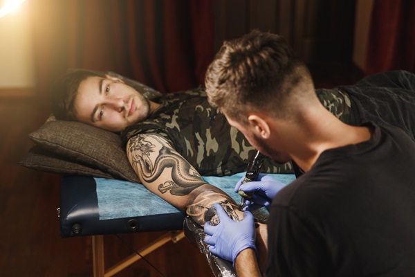 Artista profesional tatuando a un hombre en el brazo, con un diseño personalizado en tinta negra
