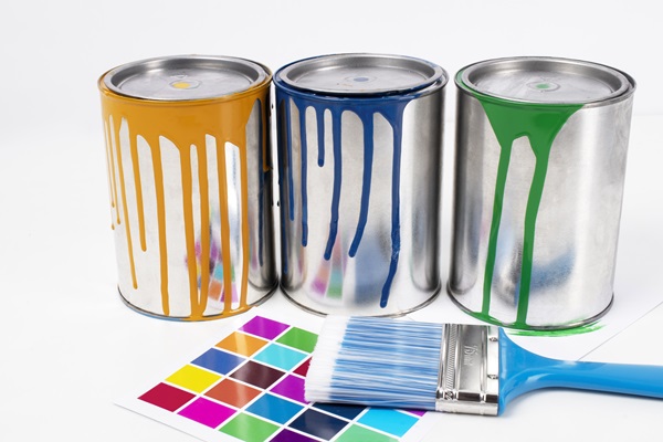 Diferentes colores de pinturas en recipientes, junto a una brocha y un catálogo con todos los colores disponibles