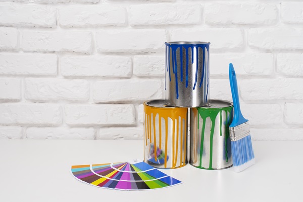 Recipientes con pinturas de colores amarillo, azul y verde, junto a una brocha y un catálogo con más colores