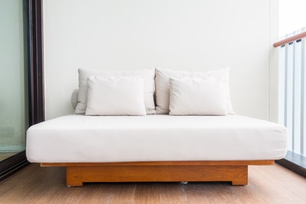 escoger un colchón de calidad y duradero - imagen de una cama con soporte de madera elevado, colchón king size y un grupo de almohadas y cojines