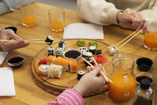 Personas comiendo diversos tipos de sushi con palillos, mojándolos en salsa de soya para realzar su sabor