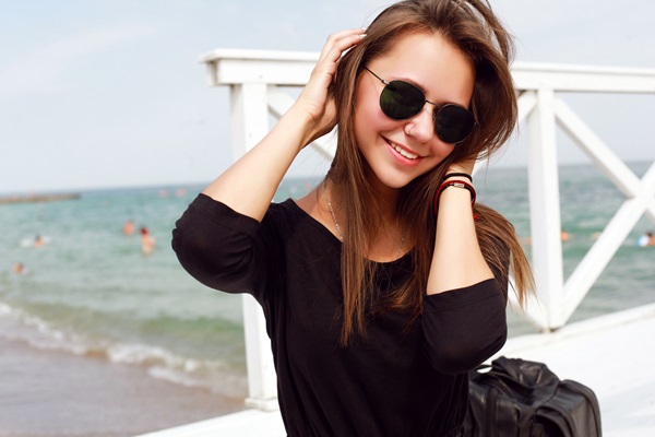Mujer posando con sus lentes oscuros en la playa, para proteger los ojos de los rayos UV