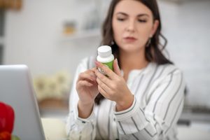 Pastillas para los sofocos de la menopausia - mujer revisando la composición de un bote de píldoras ayudada del portatil