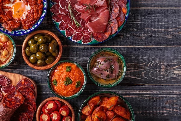 Los 10 mejores restaurantes de comida típica en Madrid - Jamón ibérico de bellota, aceitunas, patatas bravas y muchos más platos típicos de la gastronomía española servidos en una mesa de madera