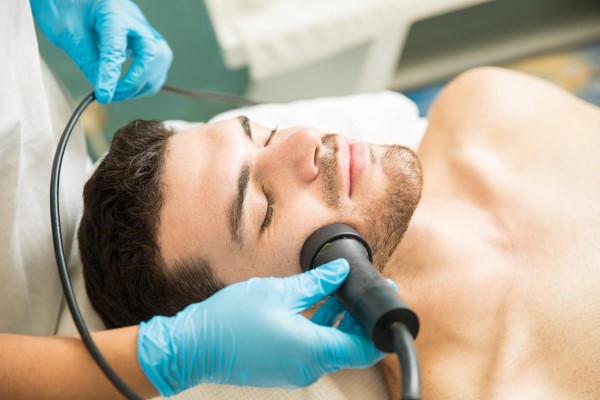 clínicas de fotorejuvenecimiento en Madrid - Especialista en medicina estética aplica sesión de radiofrecuencia para reactivar la producción de colágeno en el rostro de un hombre joven 
