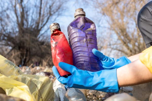 Persona con guantes recolectando varios envases de plástico que han sido tirados a la basura sin reciclar