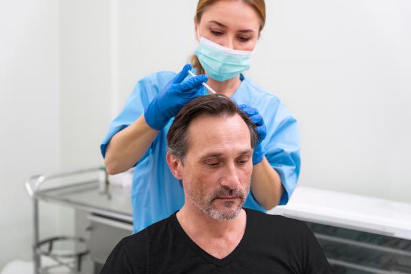 Mejores clínicas capilares en España - Médico especialista aplicando un tratamiento capilar a un paciente masculino, para estimular el crecimiento del cabello