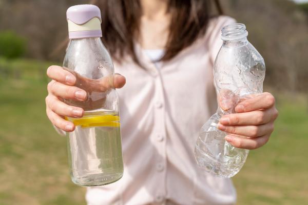 Botellas compostables - Mujer sosteniendo una botella de plástico tradicional y una botella compostable, la cual ayuda a proteger el medio ambiente