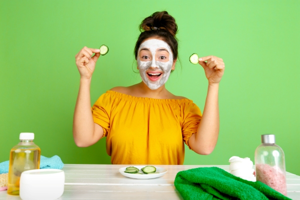 Mujer sosteniendo unos pepinillos mientras aplica una mascarilla en su rostro, para limpiar e hidratar la piel de la cara