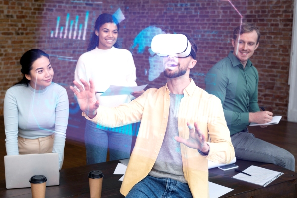 ¿Cómo funciona el metaverso? - Hombre utiliza gafas de realidad aumentada frente a compañeros de trabajo para visualizar una serie de gráficos sin necesidad de recurrir a una computadora