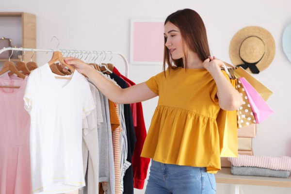 Joven con camisa mostaza carga bolsas de compra a cuestas mientras observa el diseño de una camisa blanca