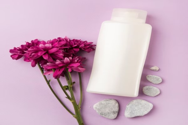 Champú sin parabenos - Imagen de un recipiente de champú junto a unas flores, las cuales le dan el olor característico de la fragancia