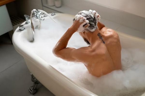 Champú sin parabenos - Hombre bañándose y lavando su cabello con un champú especial, el cual estimula el crecimiento capilar