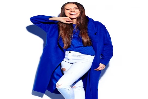Colores en tendencia - Mujer posando con un suéter de color azul elemental y un pantalón de color blanco, ofreciendo un look casual