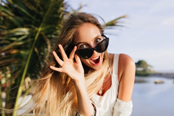 Gafas de sol - Mujer posando feliz mientras sostiene unas gafas de sol con diseño futurista, la cual la hace resaltar su estilo