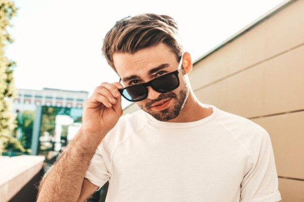 Gafas de sol - Hombre posando mientras sostiene unas gafas de sol con diseño rectangular, la cual hace resaltar su estilo y lucir más atractivo