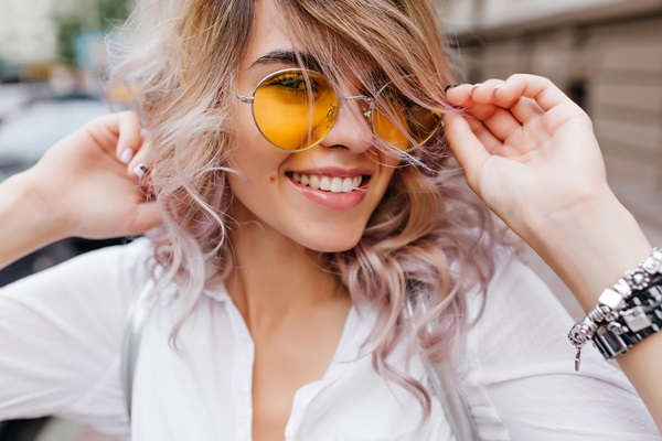 Mujer posando mientras sostiene sus lentes con diseño retro, el cual combina con su estilo y la hace lucir atractiva