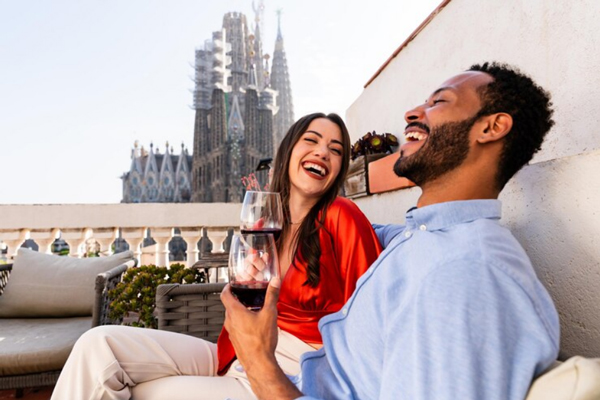 Ciudades gastronómicas de España - Pareja con copa de vino en mano disfruta de un restaurante en Barcelona con vista a la Sagrada Familia