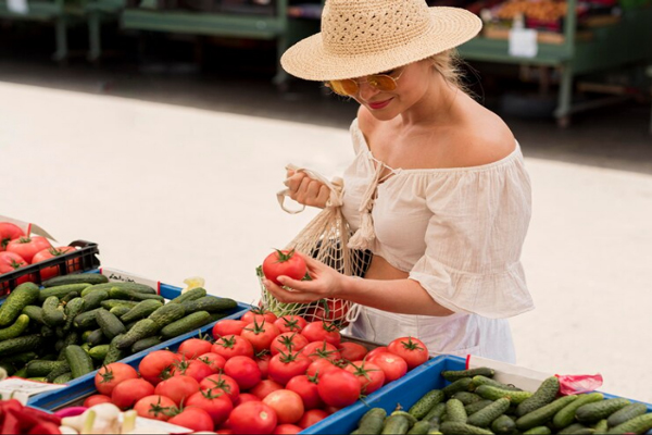 Mujer sostiene en sus manos un tomate para evaluar su calidad en un mercado de hortalizas