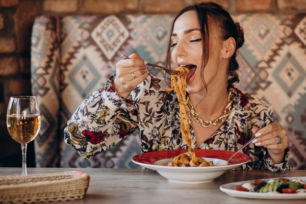Tendencias gastronómicas - Mujer joven comiendo pasta acompañada de una copa de vino en un restaurante