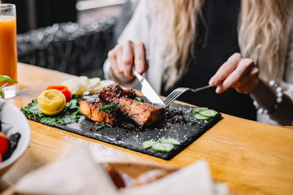 Los 10 mejores restaurantes de Madrid - Joven rubia con cuchillo y tenedor en mano disfruta de un pescado al horno con hierbas y verduras sobre la mesa
