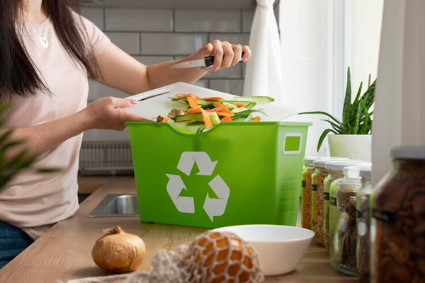 Mujer sujeta una tabla y cuchillo para colocar los residuos de alimentos en un recipiente de reciclaje