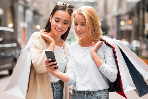 Tiendas más populares de España - Dos mujeres se detienen a revisar el móvil en la calle tras ir de compras en Madrid