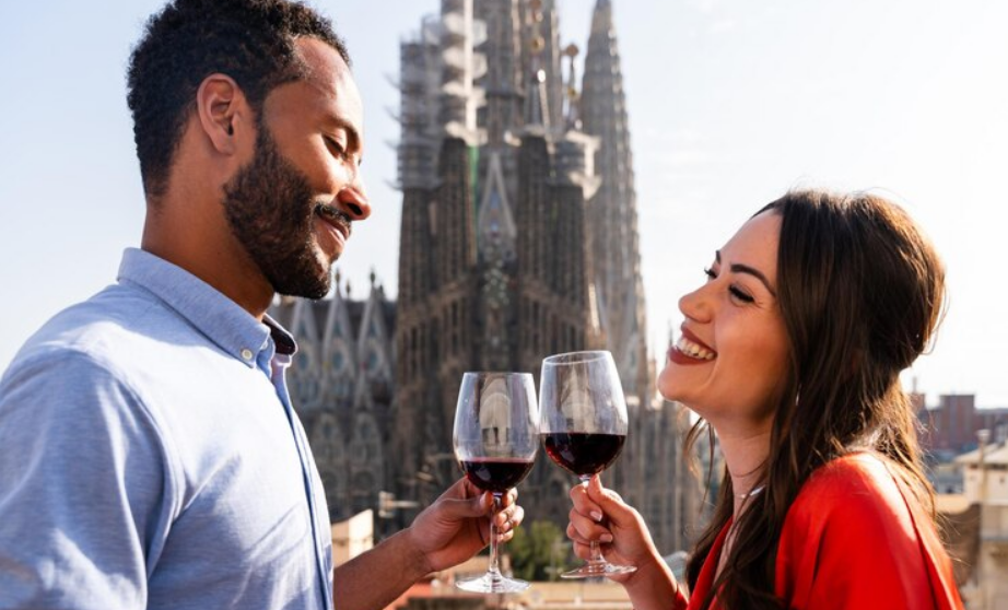 Ciudades gastronómicas de España - Pareja feliz con copa de vino brinda con la Basílica de la Sagrada Familia de fondo