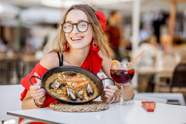 Ciudades gastronómicas de España - Joven vestida de rojo sostiene una cazuela de paella como parte de los platos típicos de Valencia