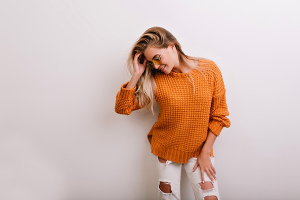 Mujer posando con un suéter de color naranja quemado y un pantalón blanco, creando un estilo divertido y casual