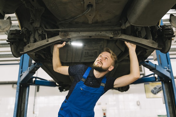 Talleres de mecánica - Mecánico sostiene una linterna mientras revisa la parte inferior de un coche en taller mecánico