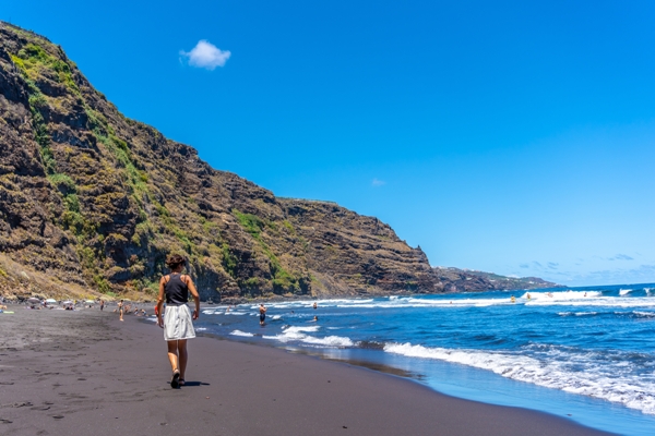 Excursiones - Mujer camina por la orilla de una playa viendo el mar