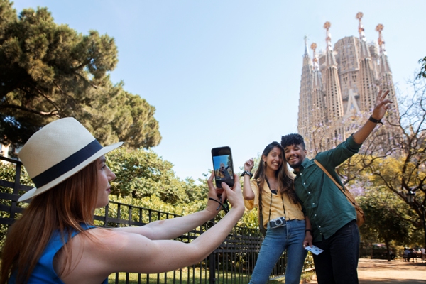 Excursiones - Mujer le toma una foto a dos personas posando frente a la Sagrada Familia de Barcelona, quienes disfrutan de excursiones cerca de Barcelona