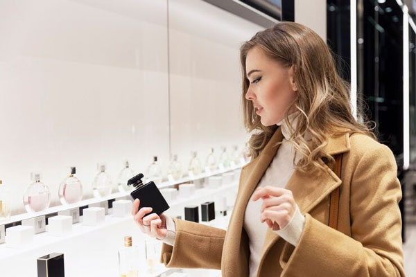 Tiendas de perfume en Madrid - Mujer con saco beige busca un aroma en específico de una determinada marca en una perfumería de Madrid