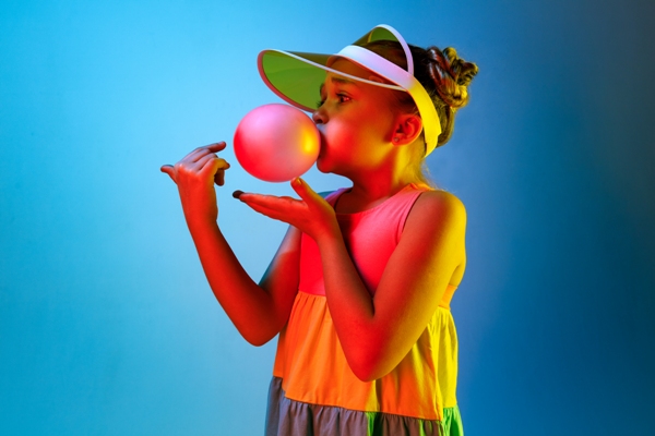 Tendencias primavera verano 2024 - Niña usando un vestido de colores mientras juega con una burbuja de chicle