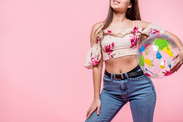 Tendencias primavera verano 2024 - Mujer posando con una blusa de estilo cut-outs mientras sujeta una pelota de playa